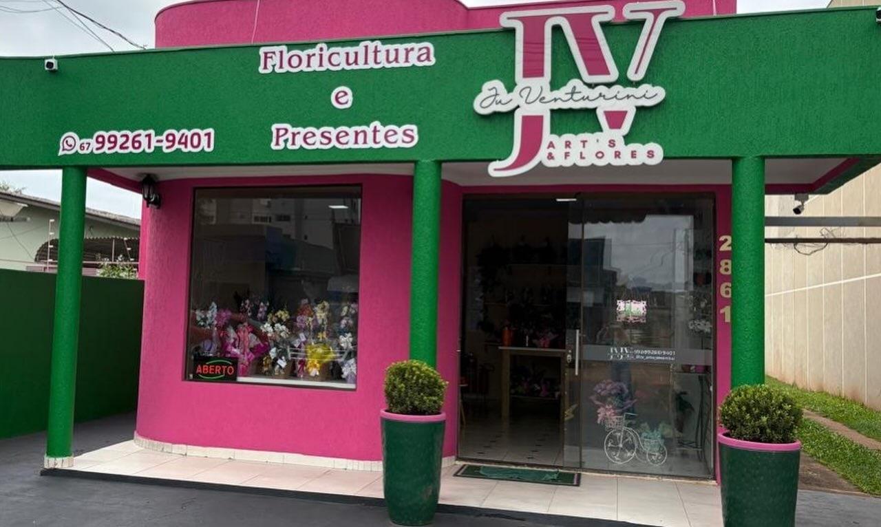 Fachada da JV Art's & Flores, pintada de rosa e verde, com a vitrine e dois vasos de buxinho na entrada