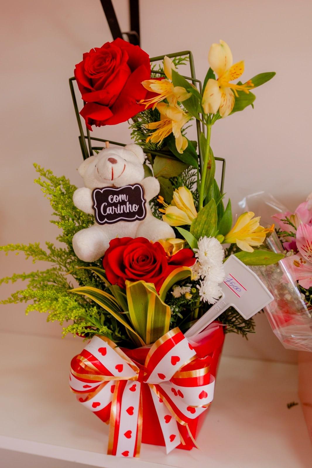 Arranjo com ursinho de pelúcia, plaquinha "com carinho", rosas vermelhas e astromélias amarelas num vaso com laço